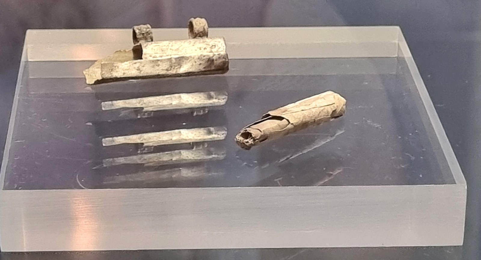 The silver capsule with its two small loops, and the rolled silver foil beside it, on a display stand in the Archaeological Museum Frankfurt